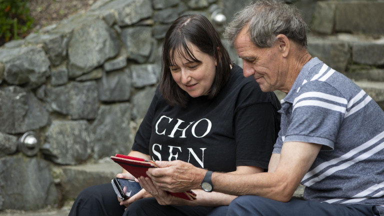 Woman and older man looking at a tablet together on some stone steps. 