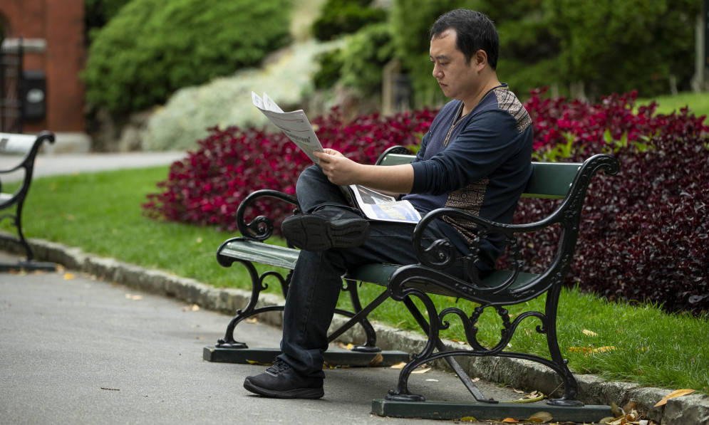 Man sitting on park bench reading newspaper